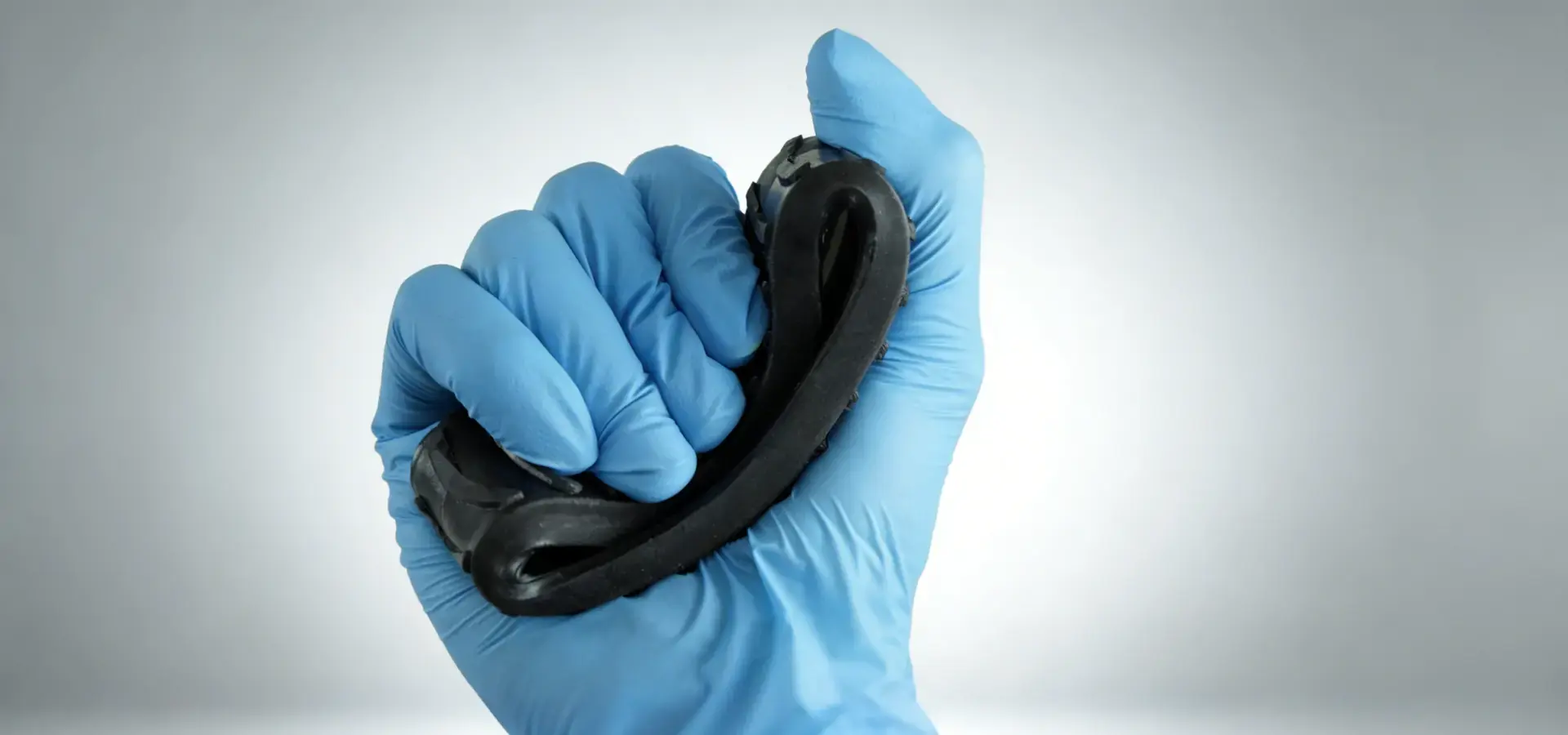 A gloved hand demonstrates the elasticity of a flexible Stereolithography (SLA) 3D printer photopolymer resin by deforming a black resin specimen, illustrating its elongation and recovery capabilities.